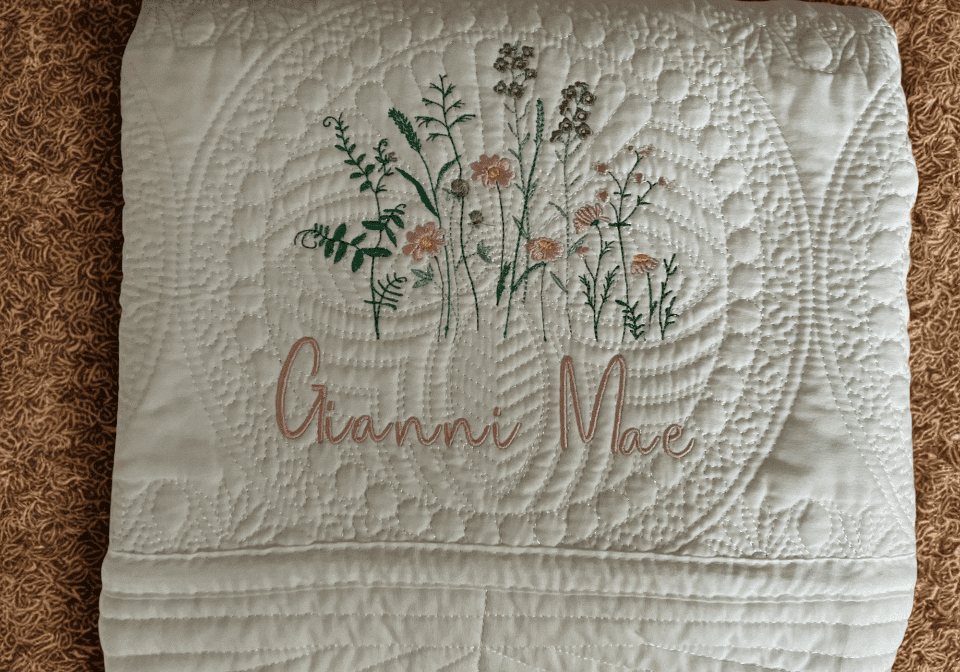 A white quilt with flowers and the name of an individual.